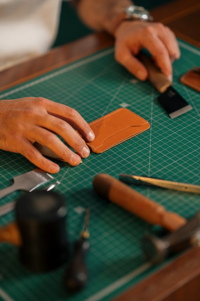 Close-up of hands crafting a leather wallet with tools on a workbench, showcasing artisan craft skills.